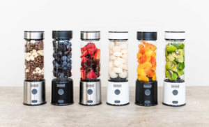 Six Zestee portable blenders in a row filled with variety fruit, nuts, seeds